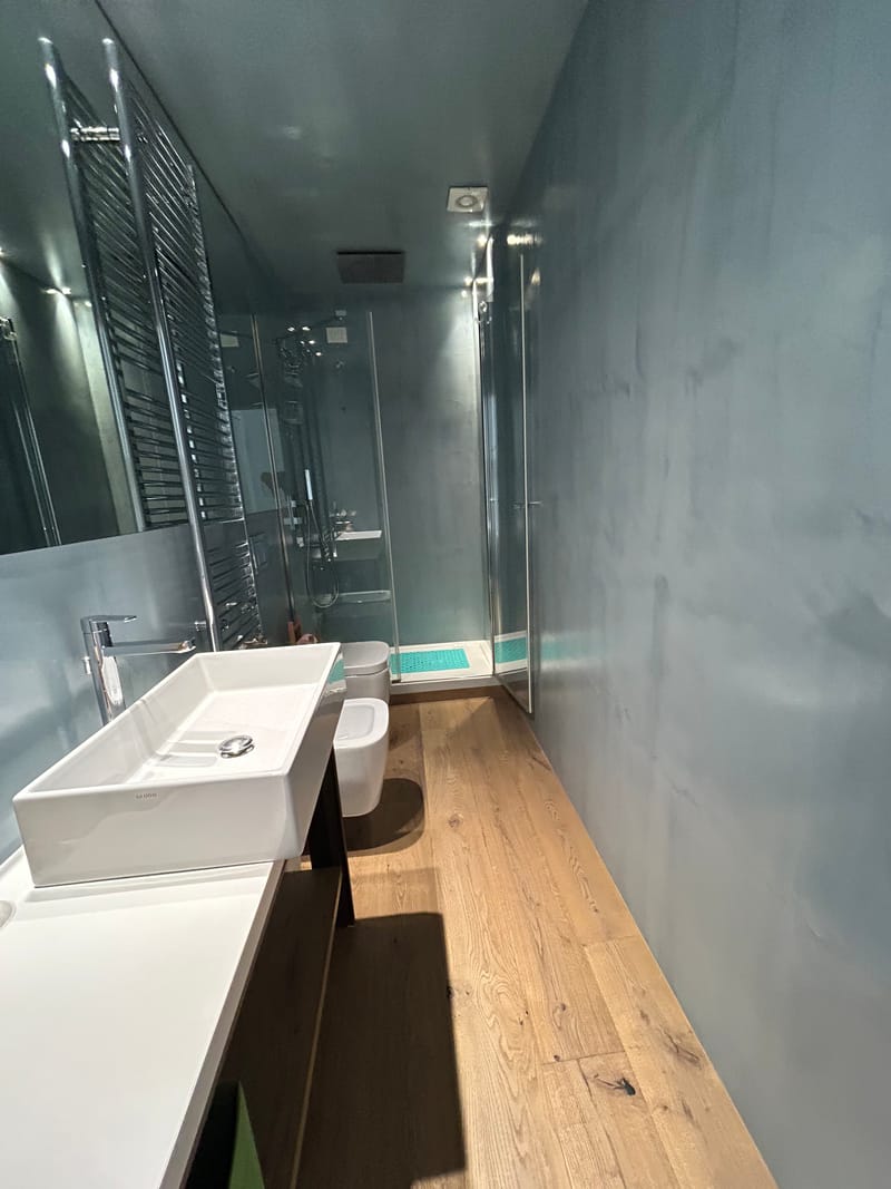 Bagno con lavabo bianco, rivestimenti grigi e doccia in vetro