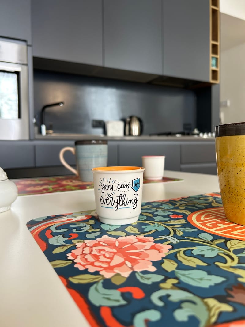 Tazza e caffettiera su una tovaglietta a fiori, davanti alla cucina