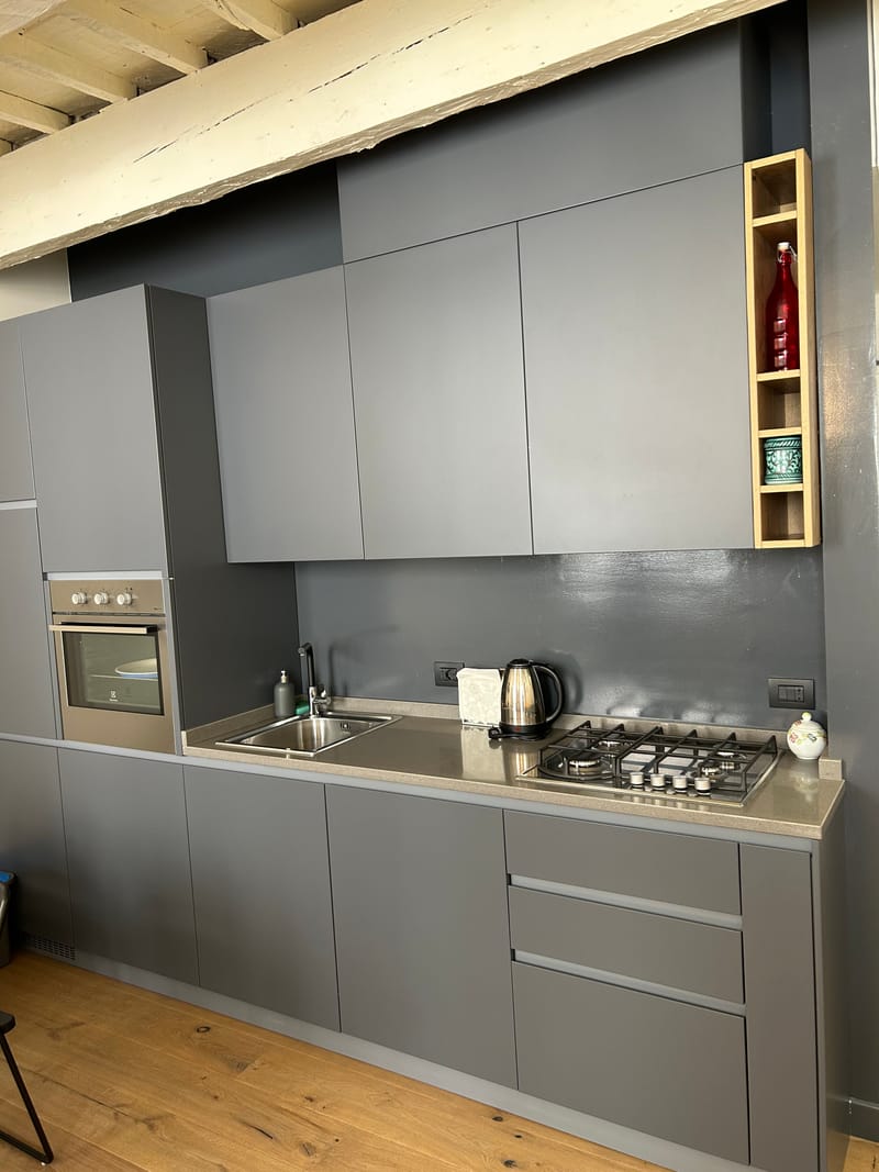 Cucina grigia con forno, piano cottura e bollitore sotto le travi in legno